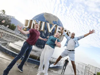 Three people jumping excitedly in front of the Universal Globe